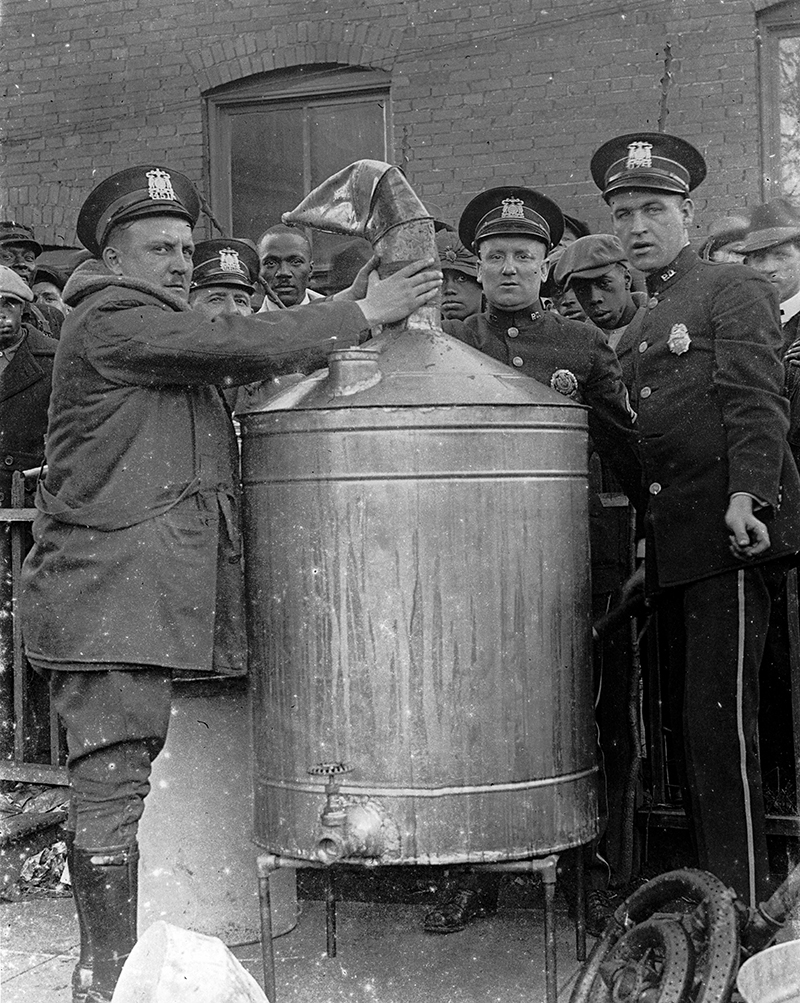 Exterior view of Kansas City police officers and crowd surrounding a confiscated still.